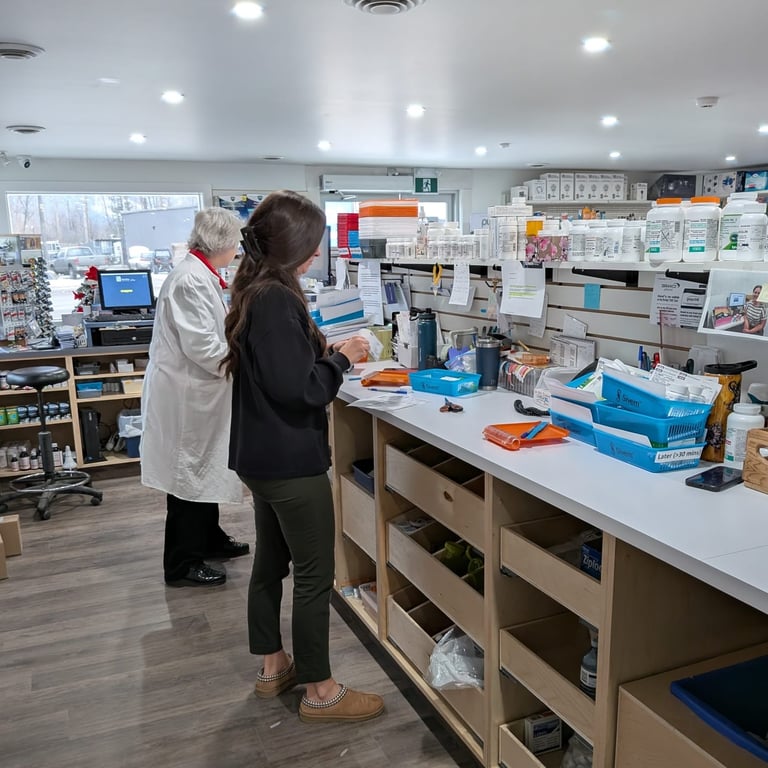 Pharmacy staff working behind the counter, organizing and preparing prescriptions with shelves of medications and supplies in the background.