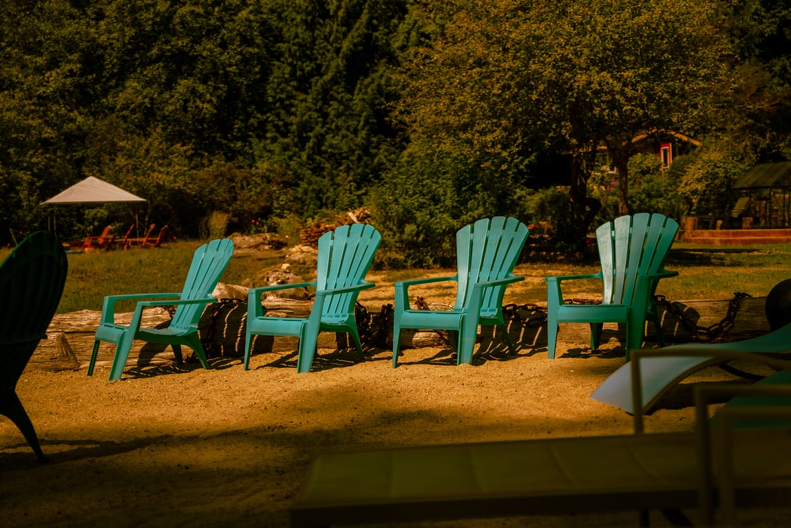 Teal Adirondack chairs facing the water on the sandy beach
