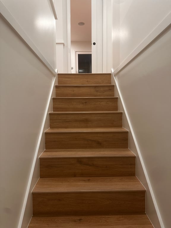 Stairwell painted in flat white with sharp lines along the stringer and casings, above new oak-look treads