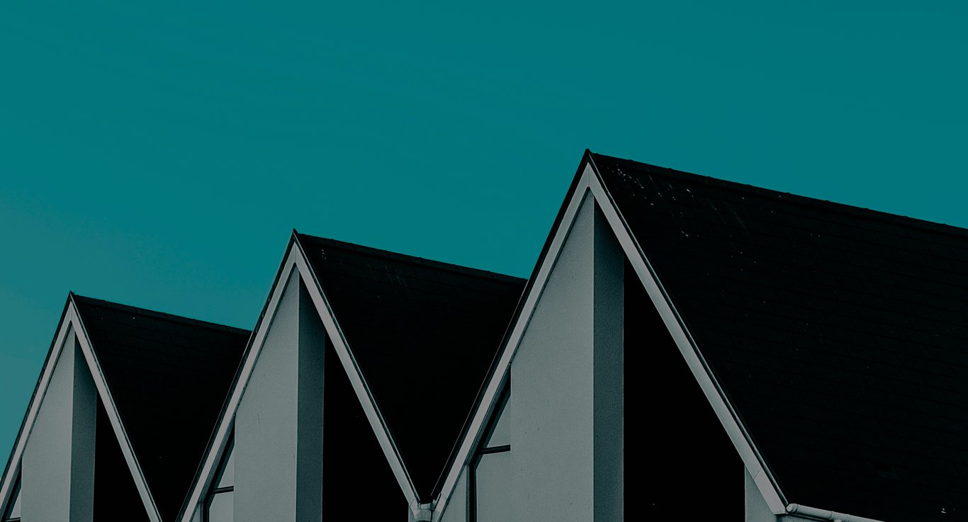 Symmetrical gable roofs of modern houses against a clear teal sky