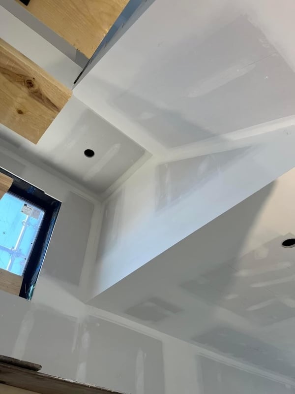 Interior view of a room under construction, showing freshly installed drywall on the walls and ceiling.