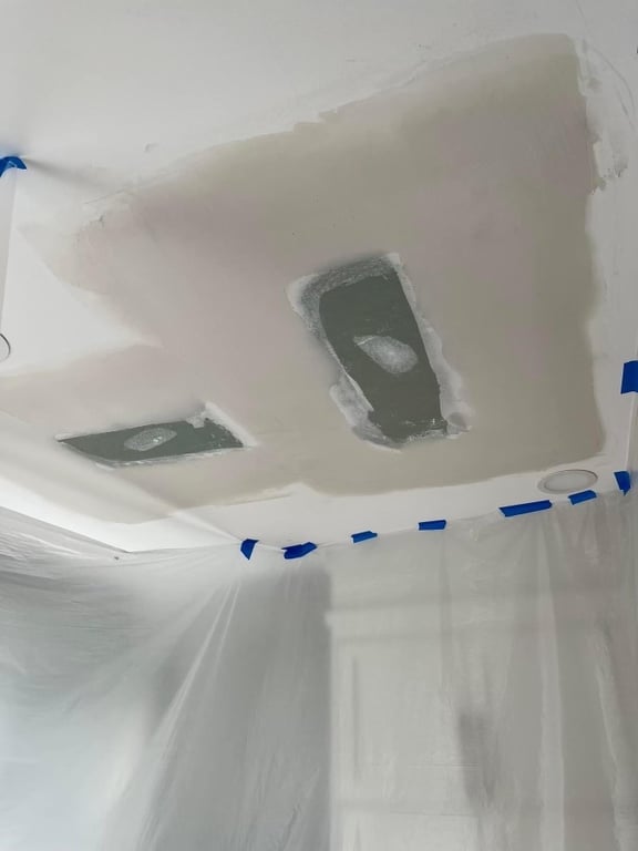 Ceiling repair in progress with patches over water-damaged areas and two recessed light cutouts, surrounded by painter's tape in preparation for finishing