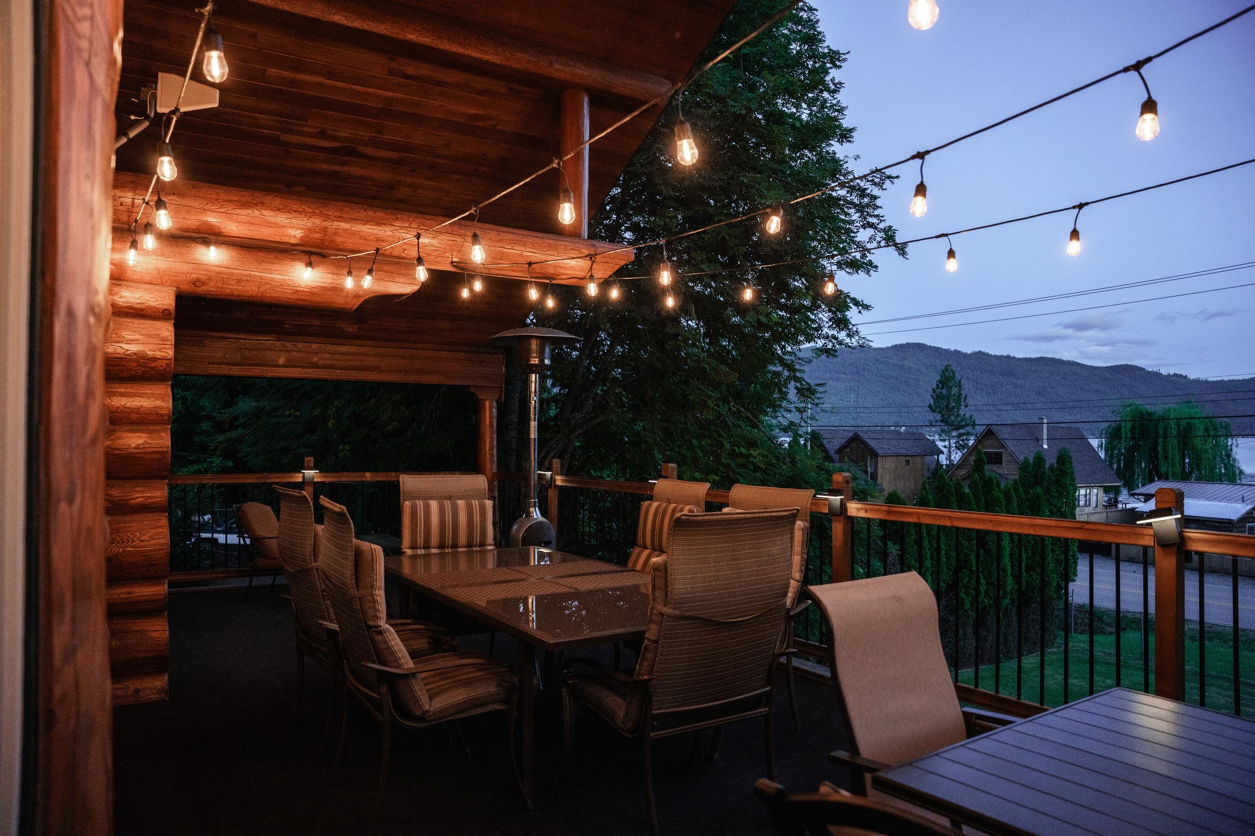 Dinner seating on the covered deck at blue hour, string lights overhead and the hills beyond the railing.