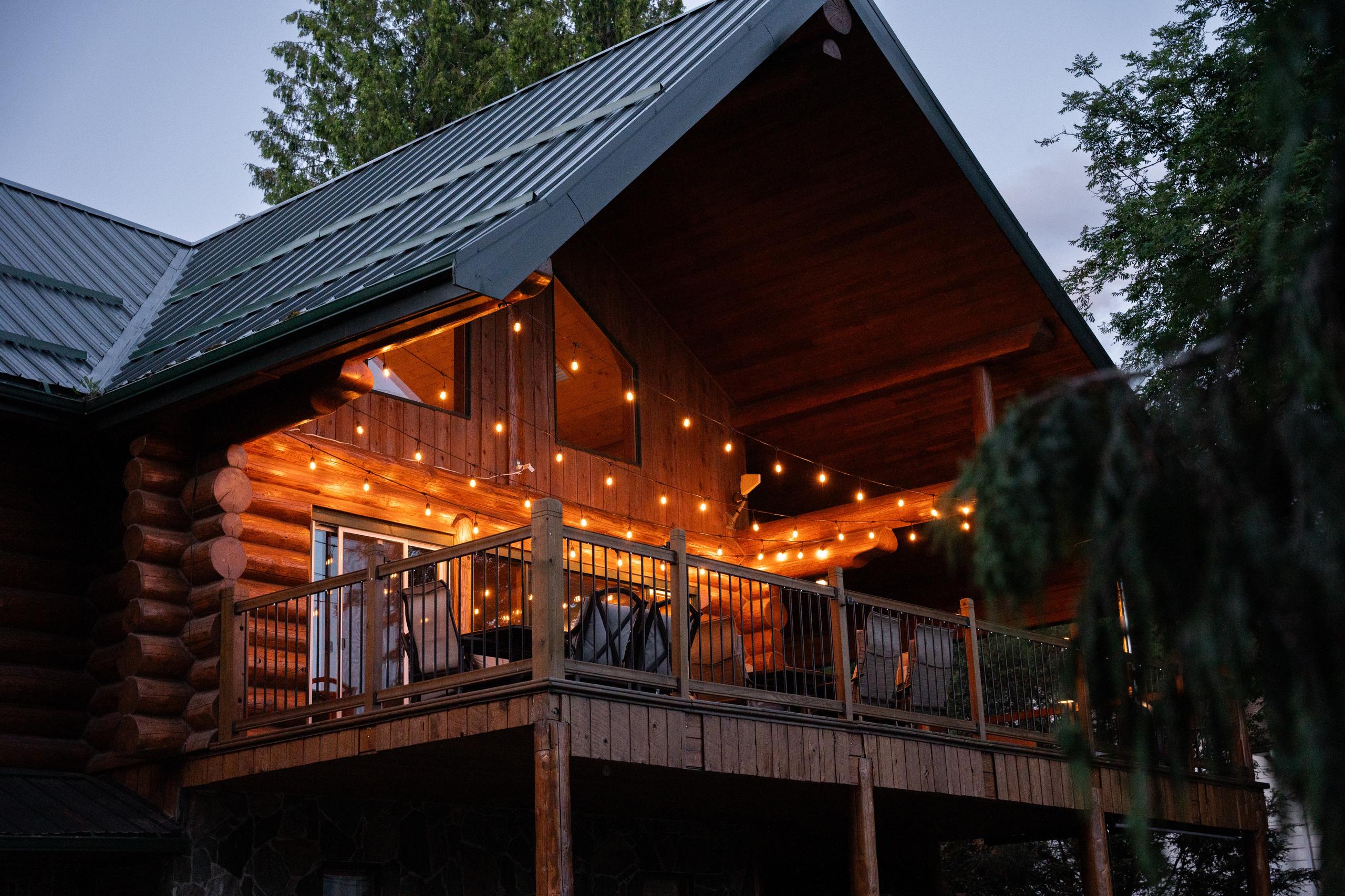 The upper deck glowing with string lights at dusk, under the peak of the log gable.