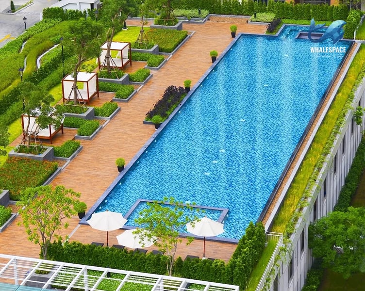 Expansive outdoor swimming pool with sun loungers, cabanas, and lush landscaping on a wooden deck