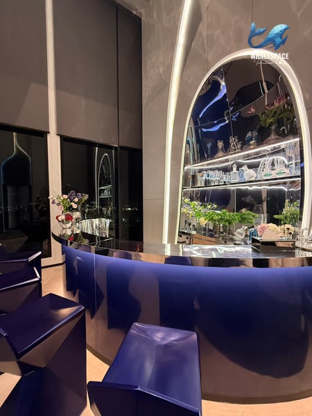 A stylish bar area with a curved blue counter, mirrored shelves filled with decor, and modern seating.