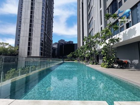 Outdoor swimming pool with tiled surface, bordered by modern high-rise buildings and sun loungers