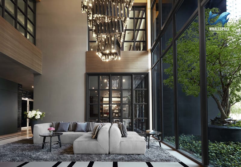 Impressive double-height lobby with a striking modern chandelier, plush lounge seating, and a full-height window overlooking a green area.