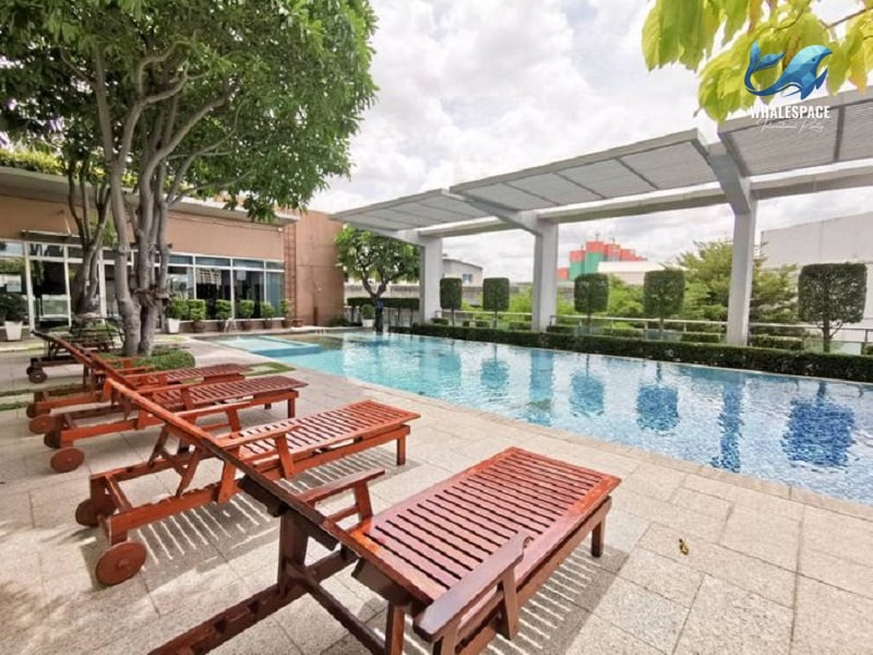 Expansive swimming pool with wooden lounge chairs and a covered seating area, surrounded by lush greenery.
