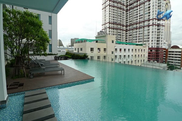Serene infinity pool with wooden deck and lounge chairs, providing breathtaking city skyline views.