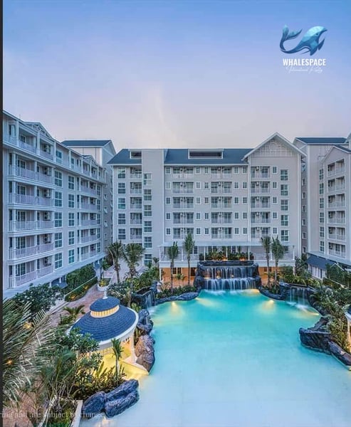 Resort-style condominium buildings overlooking a large swimming pool with decorative waterfalls and lush landscaping.