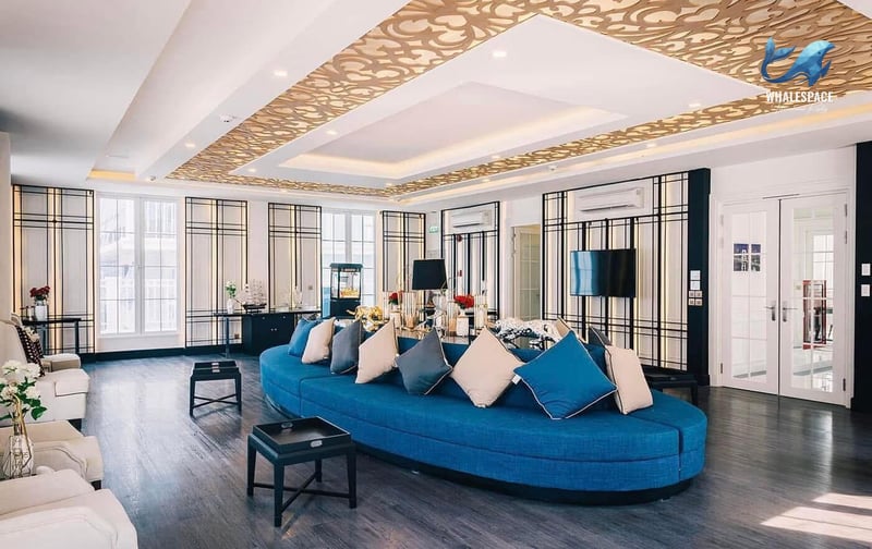Elegant residents' lounge featuring a large blue curved sofa, dark wood flooring, and an intricately patterned ceiling design.
