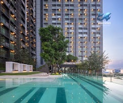 Infinity swimming pool with modern lounge seating and lush greenery, overlooking the city at dusk.