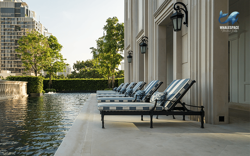 Infinity pool with striped lounge chairs overlooking a cityscape and trees, reflecting the building's classical architecture