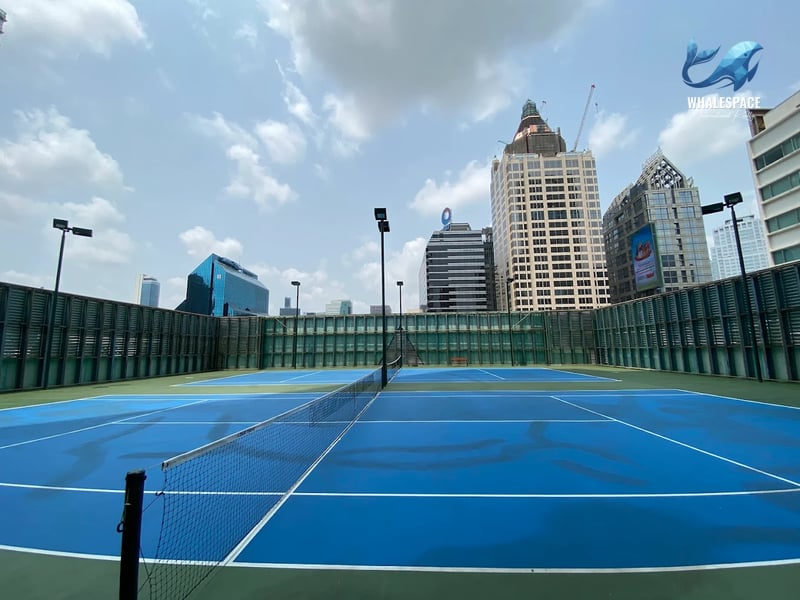 Rooftop tennis court with a bright blue playing surface and impressive city skyline views.