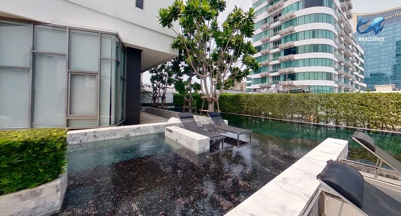Reflective shallow pool with chaise lounges and lush greenery, overlooking a modern high-rise building.