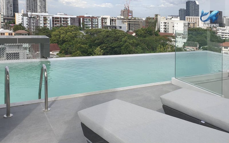 Serene infinity pool with lounge chairs on a rooftop deck, overlooking the city skyline