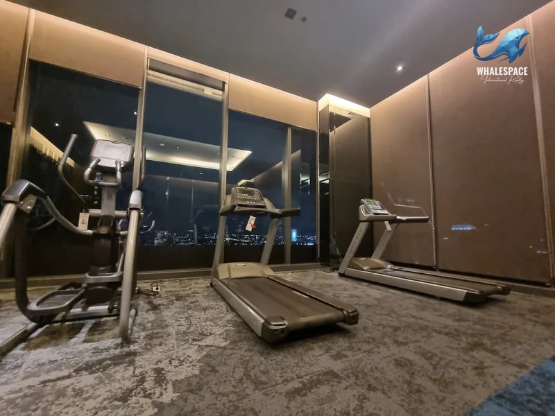 Fitness center with treadmills and an elliptical machine, offering panoramic night city views through expansive windows.