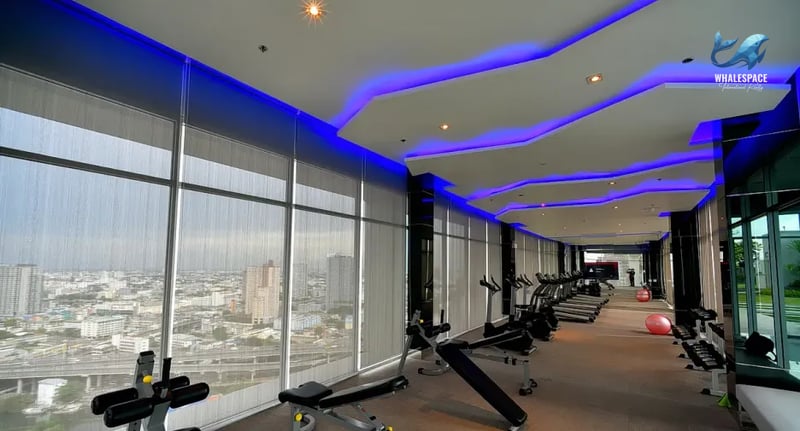 Well-equipped gymnasium with treadmills, weight benches, and free weights, illuminated by stylish blue accent lighting and offering panoramic city views.