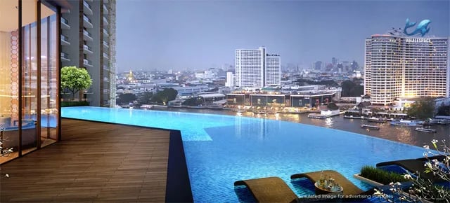 Infinity-edge swimming pool overlooking the illuminated city skyline and a wide river at dusk, with lounge chairs on a wooden deck.