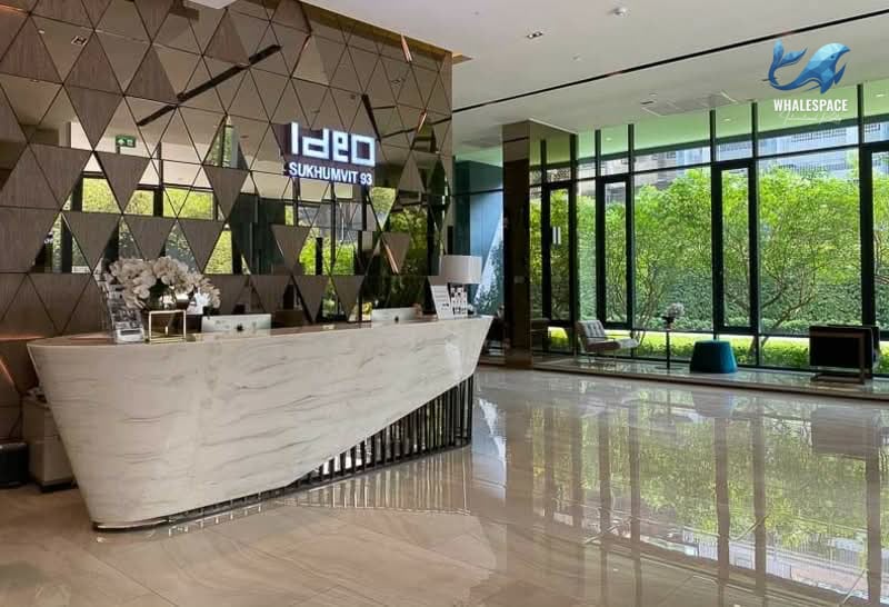 Elegant reception area with a modern marble desk and reflective geometric wall panels, featuring large windows overlooking green landscaping.