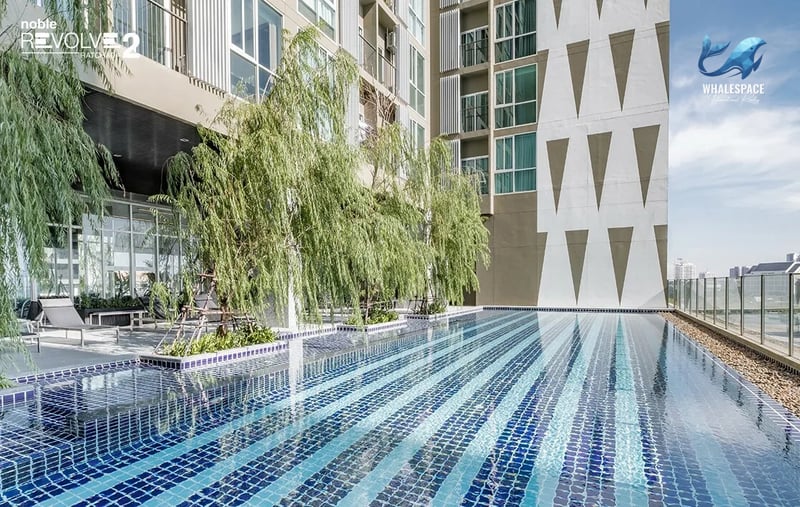 Outdoor swimming pool with blue mosaic tiles and surrounding trees, featuring a modern building exterior.