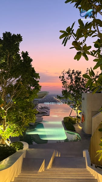 A serene infinity pool framed by trees, offering a breathtaking view of the city skyline during a colorful sunset.