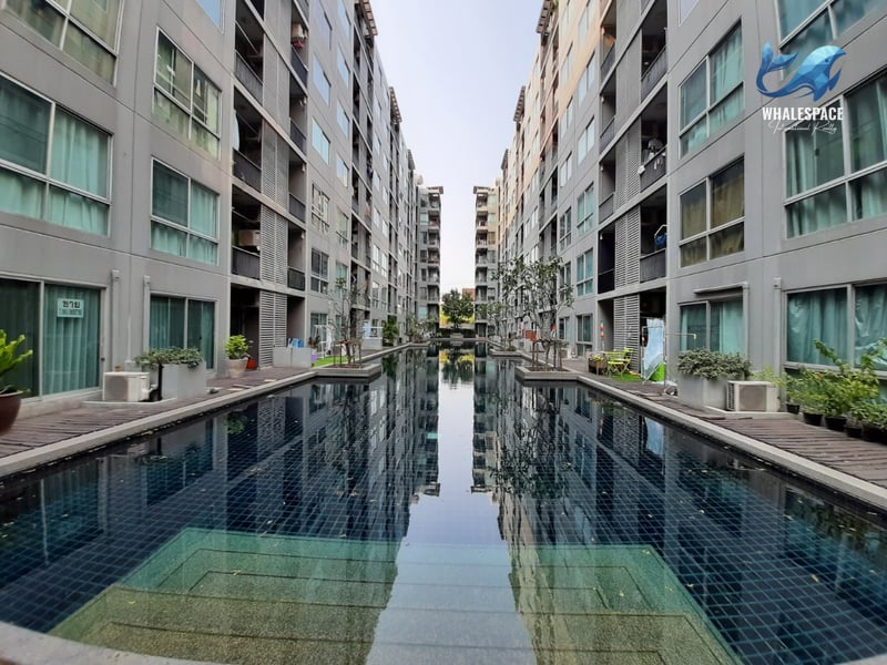 Long, reflective swimming pool set between apartment buildings, bordered by wooden decks.