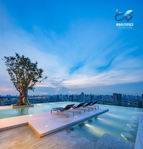 Infinity pool with lounge chairs on a rooftop deck offering panoramic city views at dusk.