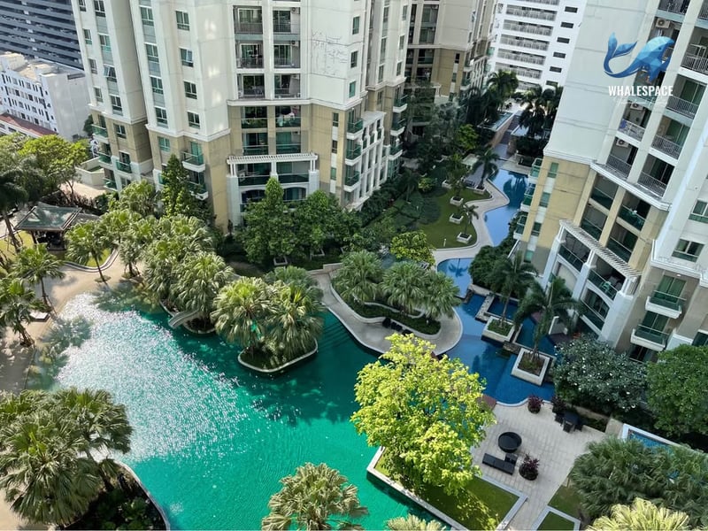 Resort-style swimming pool surrounded by lush greenery and towering buildings