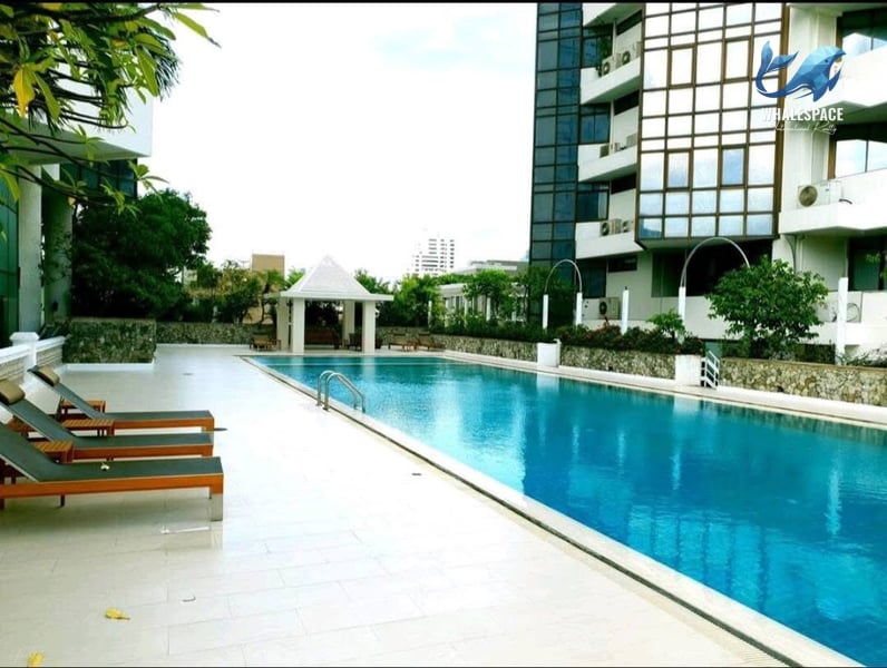 Expansive swimming pool with lounge chairs and lush greenery surrounding the deck