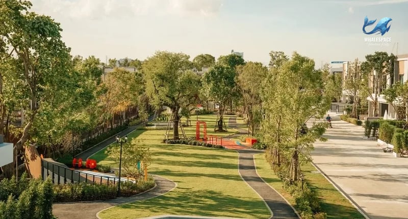 Expansive green park with walking paths, playground equipment, and surrounded by townhouses.