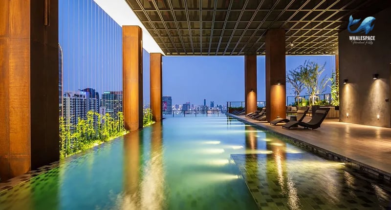 Infinity pool with panoramic city skyline views at dusk, featuring chaise lounges and a wooden deck.