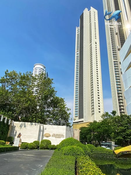 Grand entrance to the condominium complex featuring lush landscaping and a tall, modern high-rise building under a clear blue sky.