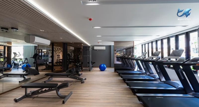 A well-equipped fitness center with treadmills, weight machines, and benches, complemented by ample natural light.