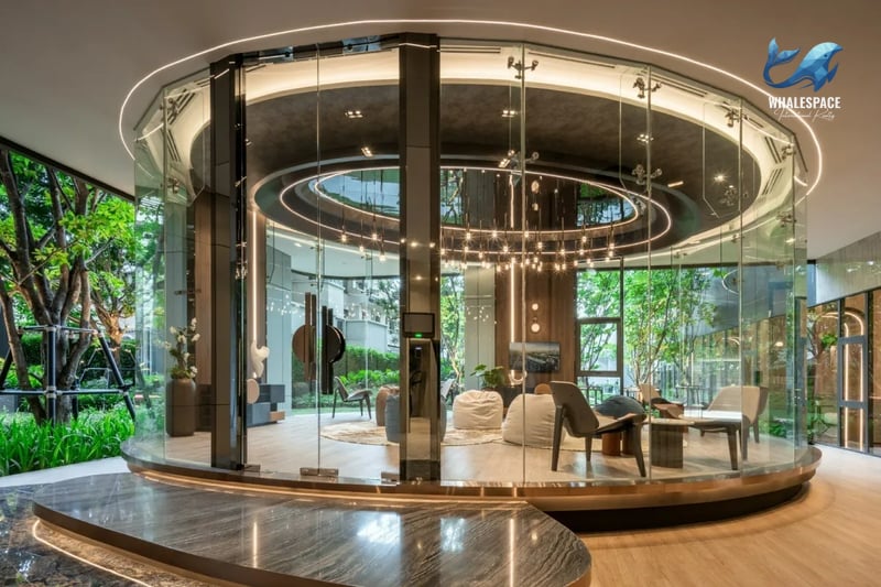 Circular glass-enclosed lounge or library area surrounded by lush garden landscaping, featuring modern seating and warm lighting