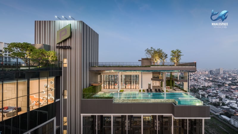 Expansive rooftop swimming pool and deck area with lounge seating, surrounded by lush greenery and city skyline.