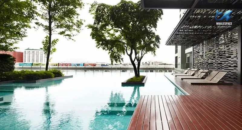 Serene swimming pool area with sleek lounge chairs and a wooden deck, surrounded by lush greenery and city views.
