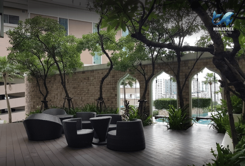 Tranquil outdoor seating area on a wooden deck, surrounded by mature trees and overlooking a swimming pool with city views.