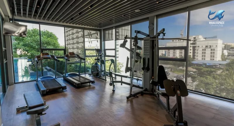 Well-equipped fitness center with treadmills and weight machines, featuring floor-to-ceiling windows overlooking green spaces.