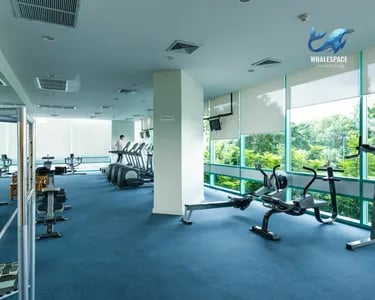 Well-equipped fitness center with various cardio and weight machines, featuring large windows overlooking lush green trees.