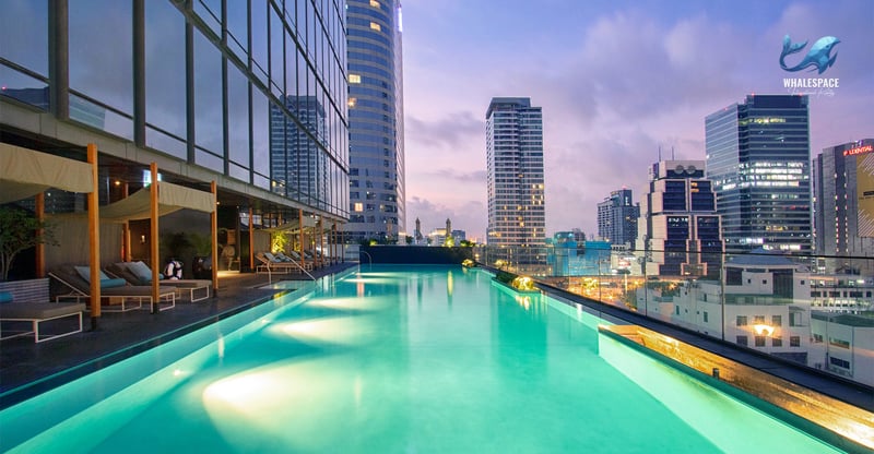 Rooftop infinity pool with city skyline views at sunset, featuring poolside lounge seating and cabanas.