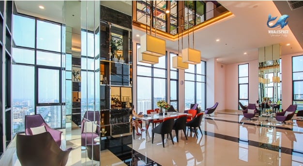 Elegant and spacious lounge area with high ceilings, luxurious seating, and floor-to-ceiling windows showcasing city vistas.
