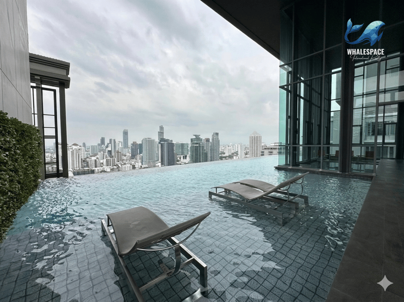 Infinity-edge swimming pool with submerged lounge chairs offering panoramic city views under a cloudy sky.