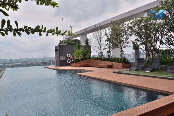Rooftop infinity pool with wooden deck, lounge chairs, and expansive city views under an open sky.