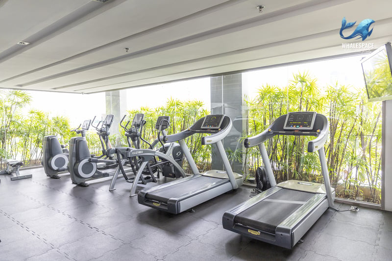 Well-equipped fitness center with treadmills and cardio machines, overlooking a bamboo garden through floor-to-ceiling windows.