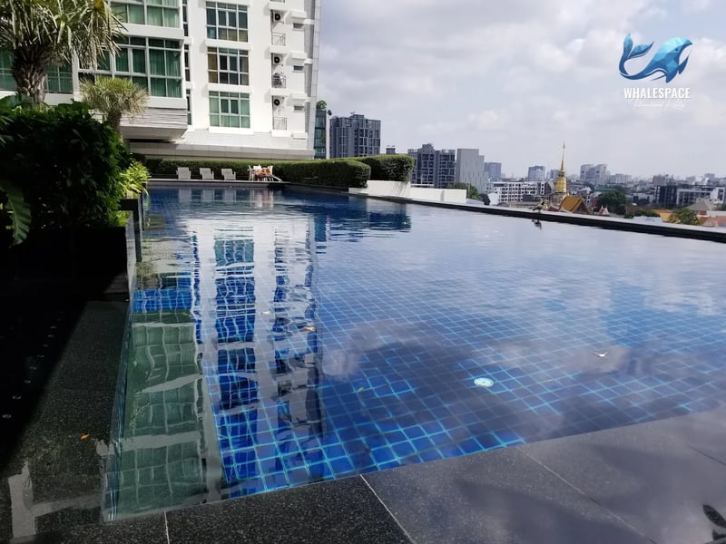 Outdoor swimming pool with blue mosaic tiles reflecting the building facade, offering a partial city view.