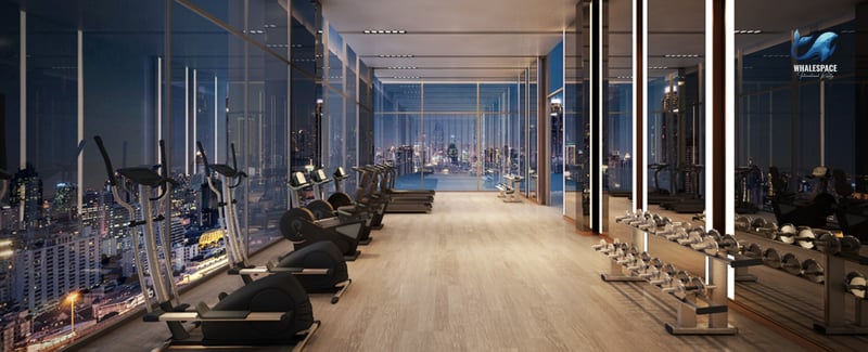 Modern fitness center with a variety of cardio and weight machines, illuminated by ceiling lights and offering panoramic city views through large windows.