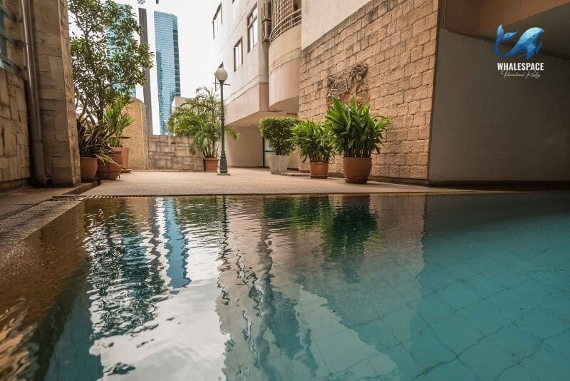 Reflective swimming pool with lush greenery and city buildings in the background