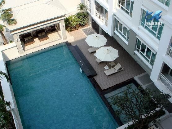 Overhead view of the outdoor swimming pool area with sun loungers, umbrellas, and a shaded seating pavilion.